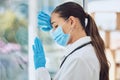 Young stressed and overworked doctor wearing mask and gloves while standing at a window in a hospital or clinic. One Royalty Free Stock Photo