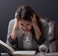 Young stressed student girl studying pile of books on library desk preparing test or exam in stress feeling