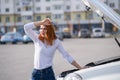 Young stressed woman driver standing near broked car with open hood