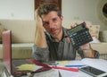 Young stressed and worried man at home living room using calculator and laptop doing domestic accounting paperwork feeling Royalty Free Stock Photo