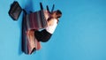 Young stressful woman, employee sitting on fallen armchair and stressfully looking on tablet against blue background