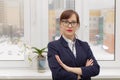 Strict business woman in a blue jacket and glasses is thinking at the window in the office at her workplace Royalty Free Stock Photo