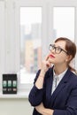 Strict business woman in a blue jacket and glasses is thinking at the window in the office at her workplace Royalty Free Stock Photo