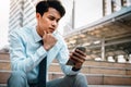 Young Striving Asian Businessman Using Mobile Phone in the City. Sitting on Staircase. Reading Seriously topic via Phone