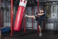 Young strong mixed martial arts fighter delivers strong straight kick to punching bag. Active exercise in gym.