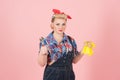 Young strong female in pin-up style dissatisfied holding yellow latex gloves and wrench isolated on pastel-pink background