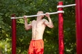 Young strong man does pull-ups on a horizontal bar on a sports ground in the summer in the city. Royalty Free Stock Photo