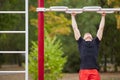 Young strong man does pull-ups on a horizontal bar on a sports ground in the summer in the city. Royalty Free Stock Photo