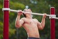 Young strong man does pull-ups on a horizontal bar on a sports ground in the summer in the city. Royalty Free Stock Photo