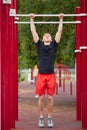 Young strong man does pull-ups on a horizontal bar on a sports ground in the summer in the city. Royalty Free Stock Photo