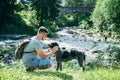 Young strong man stays near mountains river with dog and looking for the view Royalty Free Stock Photo