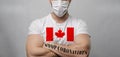 A young strong man in a white T-shirt with the image of the flag Canada crossed his arms over his chest stands on a light