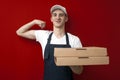 Strong pizza delivery man holds boxes and smiles, the courier shows a victory sign and delivers the order on a red background Royalty Free Stock Photo