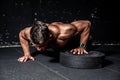 Young strong sweaty focused fit muscular man with big muscles performing push ups with one hand on the barbell weight plate for tr Royalty Free Stock Photo