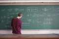 Young student in casual writing physics formula on the blackboard during study course s