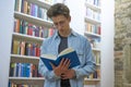 Young student with curls focussed on reading a book and standing  next to a bookshelf Royalty Free Stock Photo