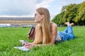 Young student girl lying on grass, educational building background