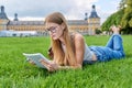 Young student girl lying on grass, educational building background