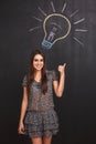 A happy young girl has an idea. Student points her finger at the lightbulb drawn on the blackboard. Royalty Free Stock Photo