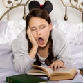 Sad young student girl reads a book while lying on a bed doing homework Royalty Free Stock Photo