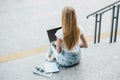 Young student girl uses laptop with white screen, sitting on stairs and looking at empty black monitor screen near Royalty Free Stock Photo