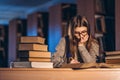 Young student in glasses preparing for the exam. Girl in the evening sits at a table in the library with a pile of books Royalty Free Stock Photo