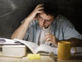 Young student at home desk reading biting pen studying at night with pile of books and coffee Royalty Free Stock Photo