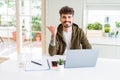 Young student man using computer laptop and notebook pointing and showing with thumb up to the side with happy face smiling Royalty Free Stock Photo