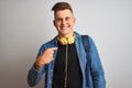 Young student man wearing denim shirt backpack headphones over isolated white background with surprise face pointing finger to Royalty Free Stock Photo