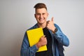 Young student man wearing denim shirt backpack notebook over isolated white background happy with big smile doing ok sign, thumb Royalty Free Stock Photo