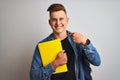 Young student man wearing denim shirt backpack notebook over isolated white background with surprise face pointing finger to Royalty Free Stock Photo