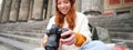 Young student, photographer sits on street stairs and checks her shots on professional camera, taking photos outdoors Royalty Free Stock Photo