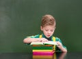 Young student reading a book near empty green chalkboard