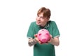 a young student of a red-haired man in a green t-shirt with a tattoo on his arm accumulated money in a piggy bank Royalty Free Stock Photo