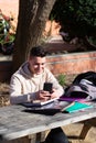 Young student sitting in a park while using a mobile phone on a wooden table Royalty Free Stock Photo