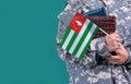Young student soldier in uniform with books holds in hand Abkhazia flag, close up