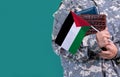 Young student soldier in uniform with books holds in hand Palestine flag, close up