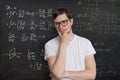 Young student is solving math exam. Mathematics formular on blackboard in background