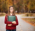 Young student with surprised face looks out of folder in red checkered shirt. Portrait of clever young woman