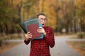 Young student with surprised face looks out of folder in red checkered shirt. Portrait of handsome young man holding folders Royalty Free Stock Photo