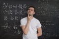 Young student is thinking and solving mathematical problem. Math formular on blackboard in background Royalty Free Stock Photo