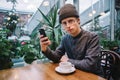 Young student uses a mobile phone in a nice cafe near the window. tea is on the table, and outside greenhouse Royalty Free Stock Photo