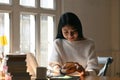 Young student woman sitting in the library with a pile of books and using mobile phone. Royalty Free Stock Photo