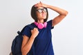 Young student woman wearing backpack glasses headphones over isolated white background stressed with hand on head, shocked with Royalty Free Stock Photo