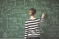 Young student writing with chalk on green chalk board in classroom