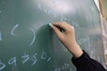 Young student writing mathematical equations on a green chalkboard