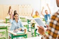 young students raising up hands to answer on teachers question while he standing with tablet