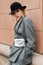 Young stylish beautiful woman fashion model is posing in street, wearing pantsuit, having purse on her waist Royalty Free Stock Photo