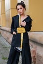 Young stylish beautiful woman fashion model is posing in street, wearing pantsuit, having purse on her waist Royalty Free Stock Photo