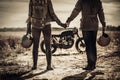 Young, stylish cafe racer couple and vintage custom motorcycles in field Royalty Free Stock Photo